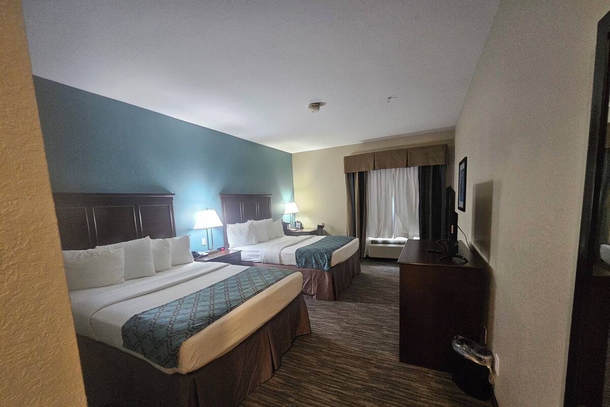 Une chambre d’hôtel avec deux lits, un bureau, une chaise, une télévision et une fenêtre avec des rideaux.