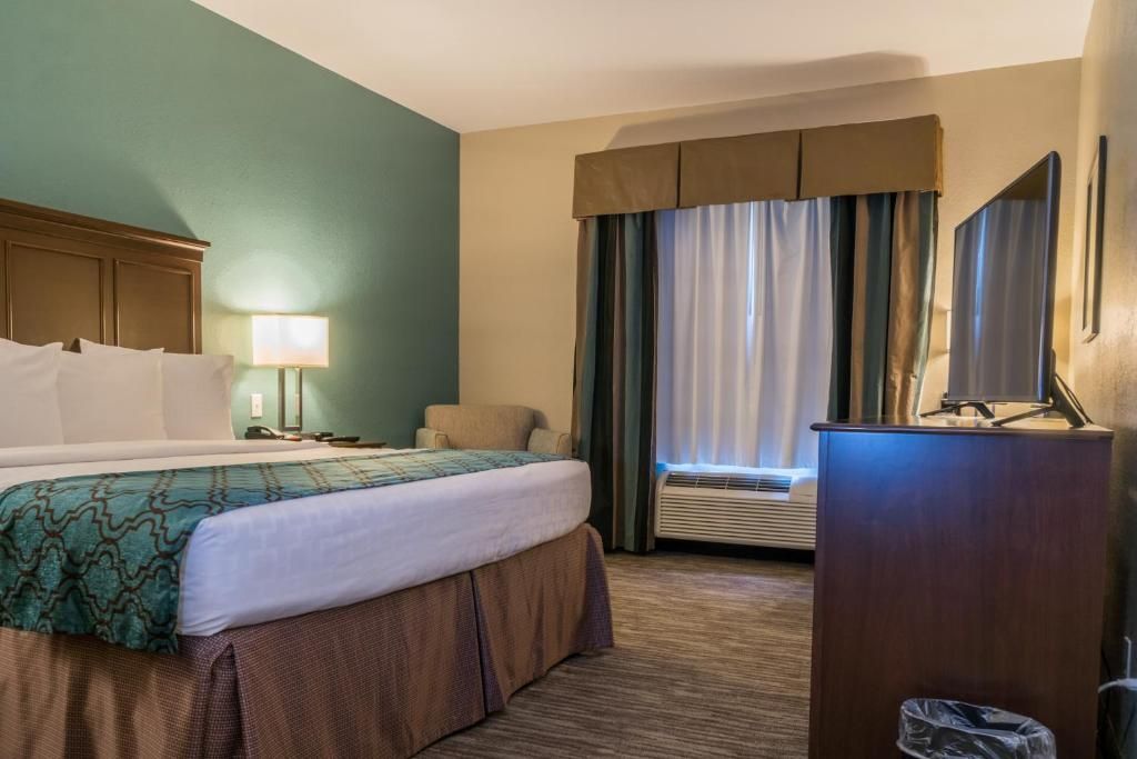 A hotel room with a bed, a desk, a chair, a lamp, and a window with curtains.