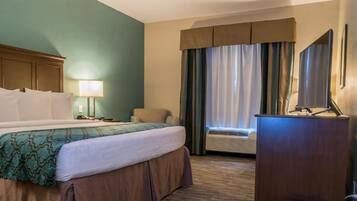 A hotel room with a bed, a desk, a chair, a lamp, and a window with curtains.