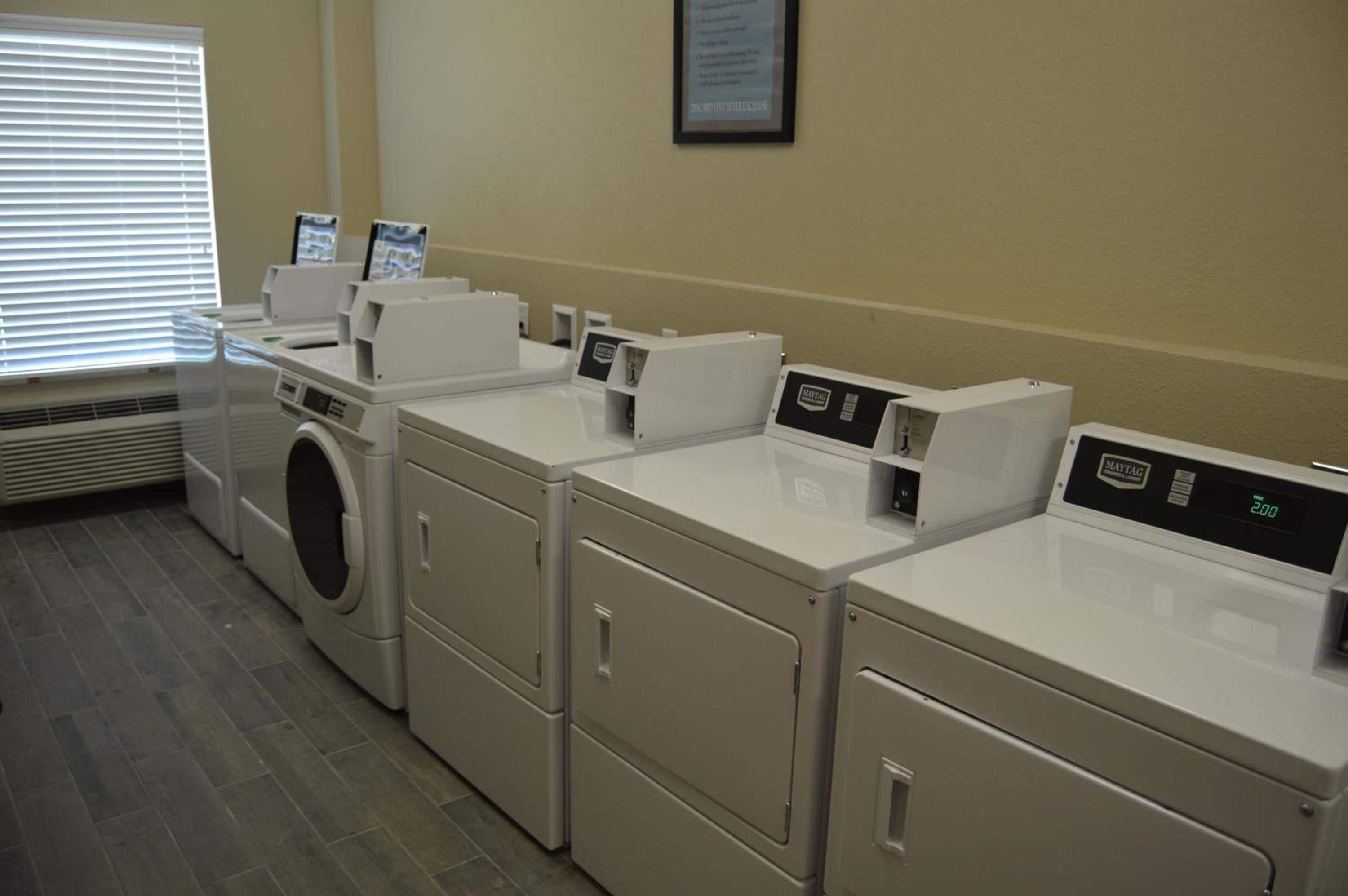 A laundry facility with multiple washing machines and dryers, a vent, and a framed sign on the wall.