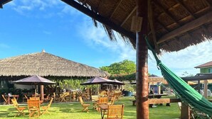 Un espace extérieur doté d’une terrasse en bois, de structures à toits de chaume et d’un hamac.