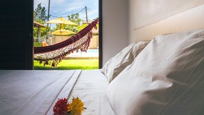 Un lit avec du linge de lit blanc, un hamac à l’extérieur de la fenêtre et une vue sur une piscine et la verdure.