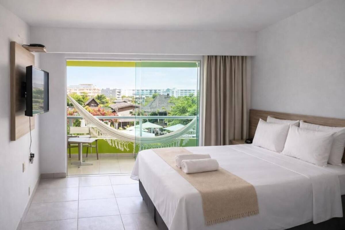 Une chambre d’hôtel avec un lit, une télévision, un balcon avec un hamac et une vue sur les bâtiments.