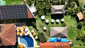 Un espace piscine aménagé sur le toit, avec des parasols, une structure à toit de chaume et des panneaux solaires.
