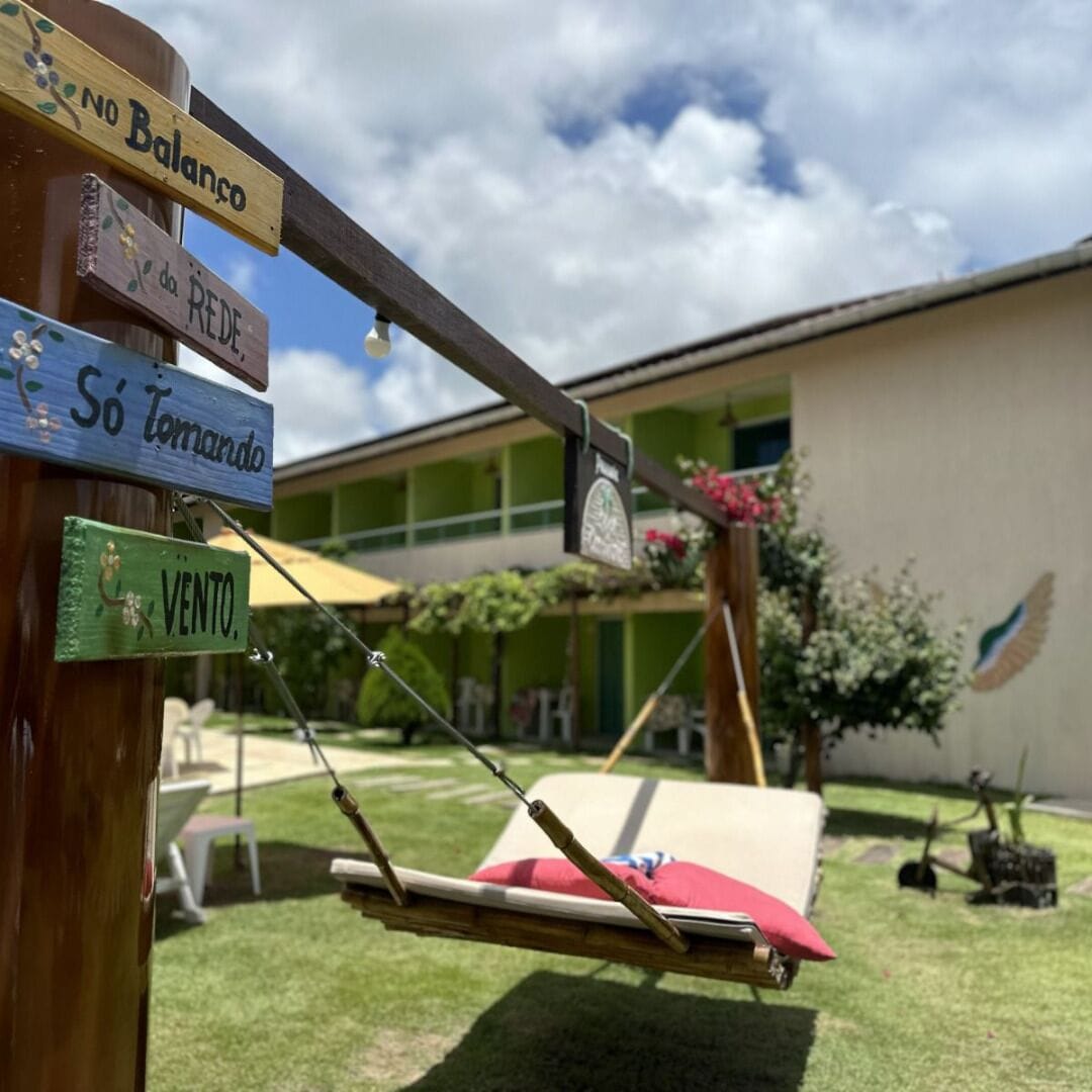 Une balançoire en bois avec un coussin rouge, un hamac et un panneau indicateur avec plusieurs panneaux.