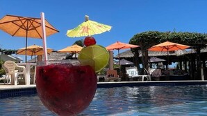 Un cadre agréable au bord de la piscine, avec un verre d’une boisson rouge, des parasols et des chaises longues.