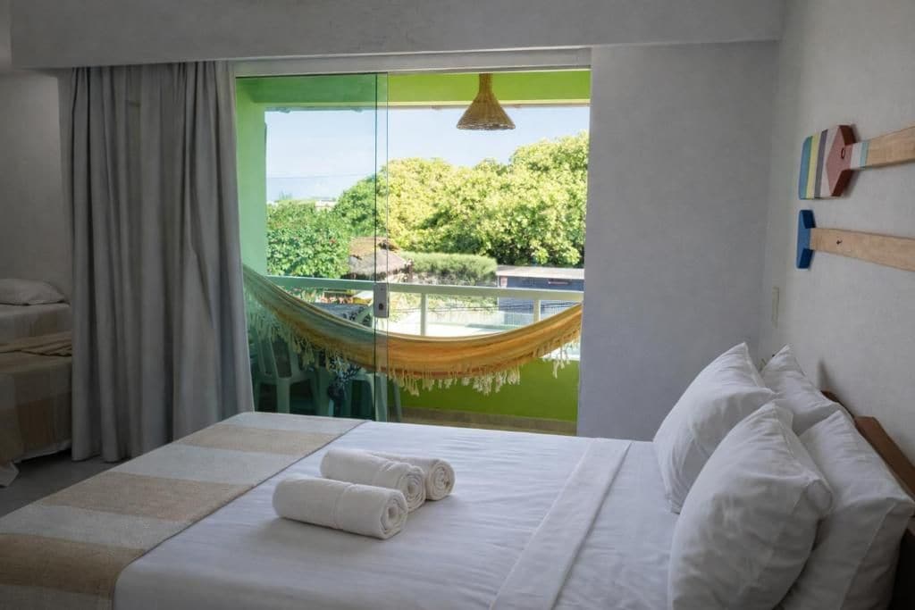 Ett hotellrum med en säng, en hängmatta och utsikt över grönområden utanför.