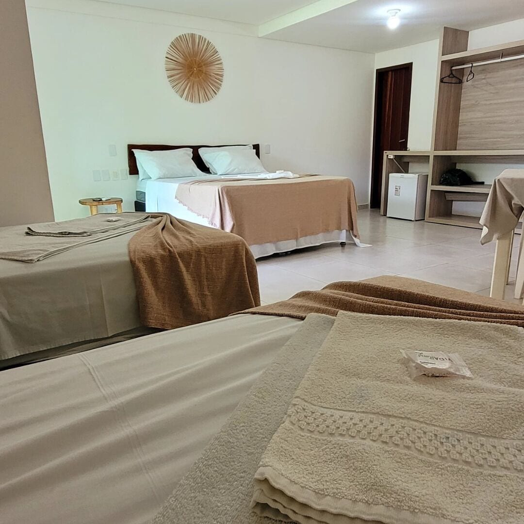 A hotel room with two beds, a small table, and a wall-mounted shelf.