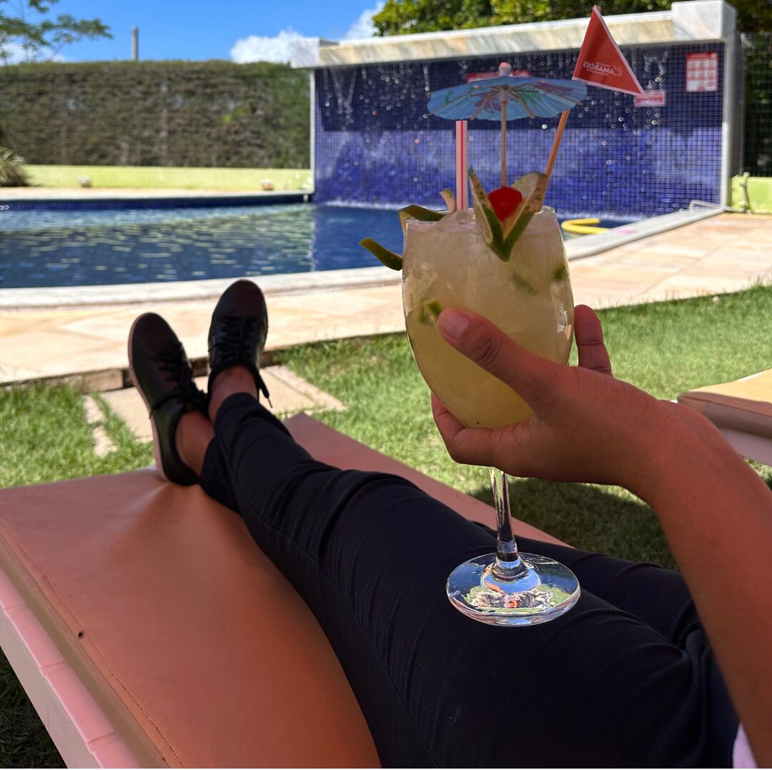 Une personne se détend au bord d’une piscine, un verre à la main.