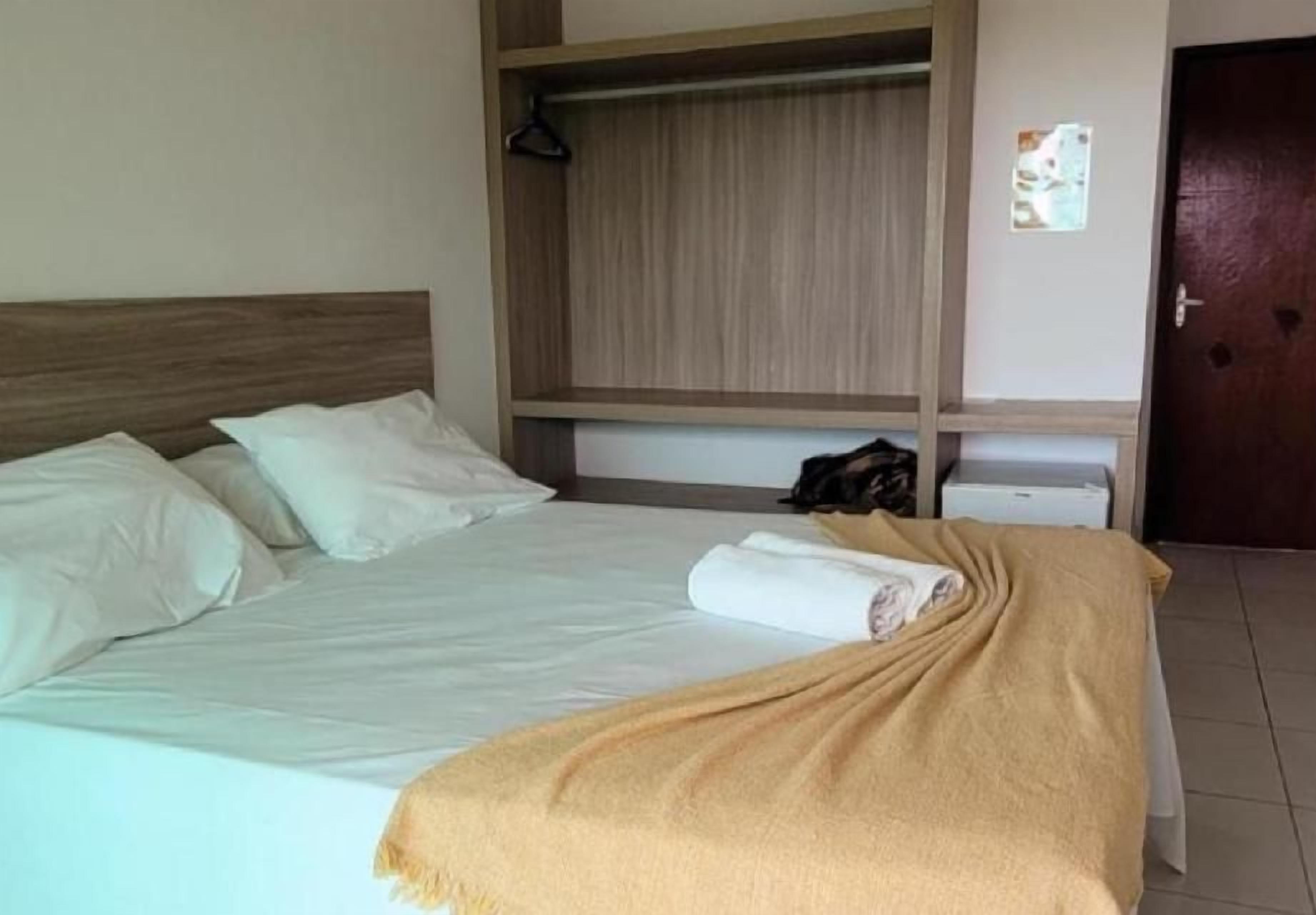 Une chambre d’hôtel avec un lit, une armoire en bois, un petit bureau et une porte.