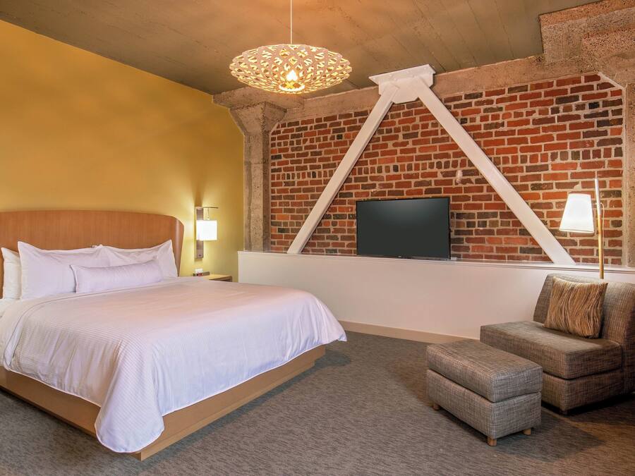 A bedroom with a brick wall, a bed, a TV, and a small seating area.