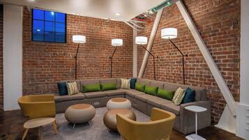 A modern lounge area with a brick wall, a sectional sofa with cushions, round ottomans, and floor lamps.