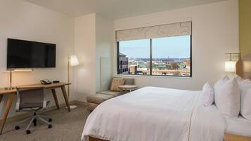 A hotel room with a large bed, a desk with a chair, a television, and a window offering a city view.
