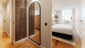 Een slaapkamer met een bed, houten vloer, een spiegel en een garderobe met schuifdeuren.