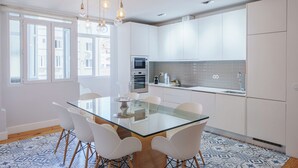 Een moderne keuken met witte kasten, een eettafel met glazen blad en een vloer met patroon.