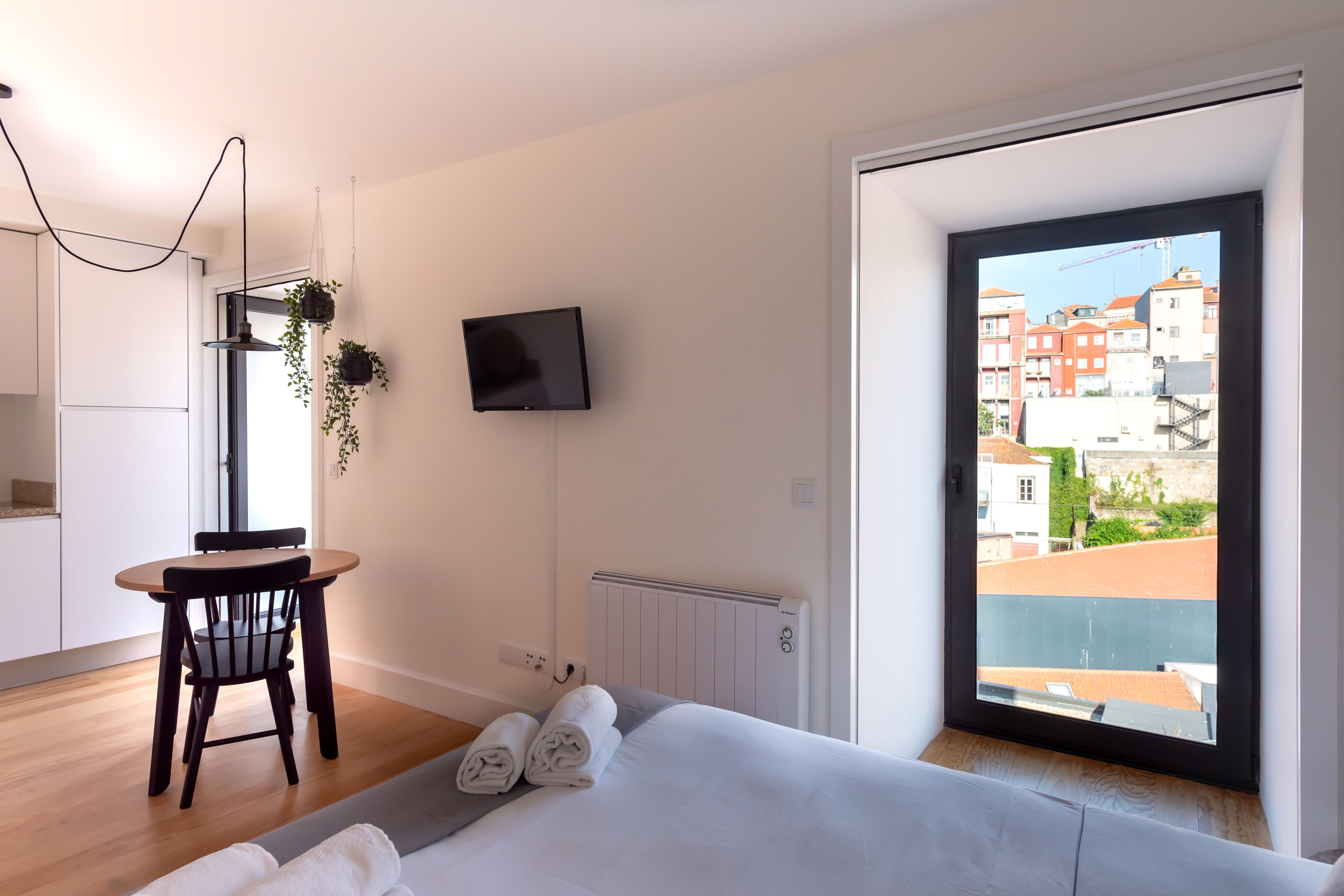 Une chambre d’hôtel moderne, équipée d’un lit, d’une petite table avec des chaises, d’une télévision et offrant une vue sur les bâtiments à travers une grande fenêtre.