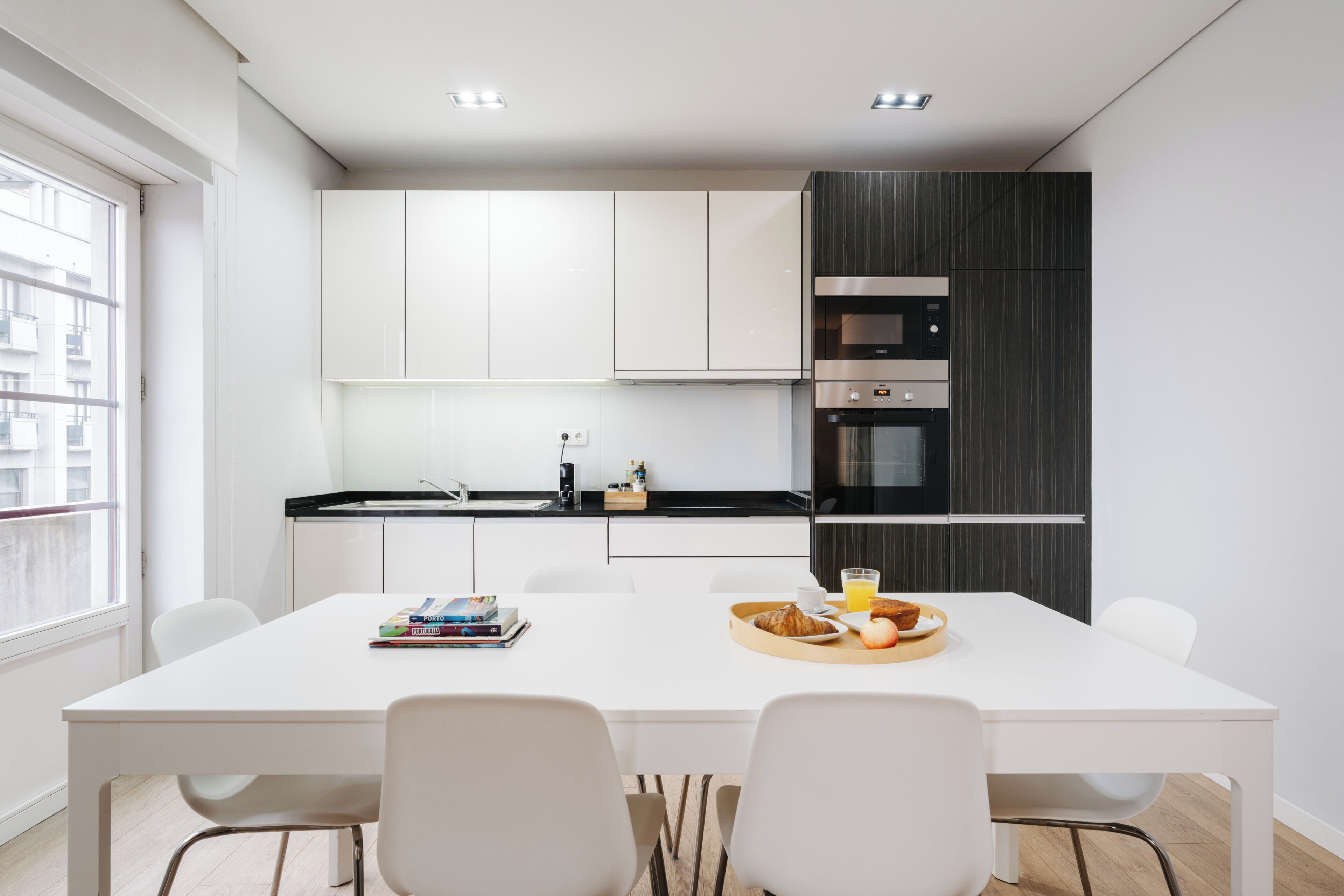 A modern kitchen with white cabinets, a black countertop, and a dining area with a white table and chairs.