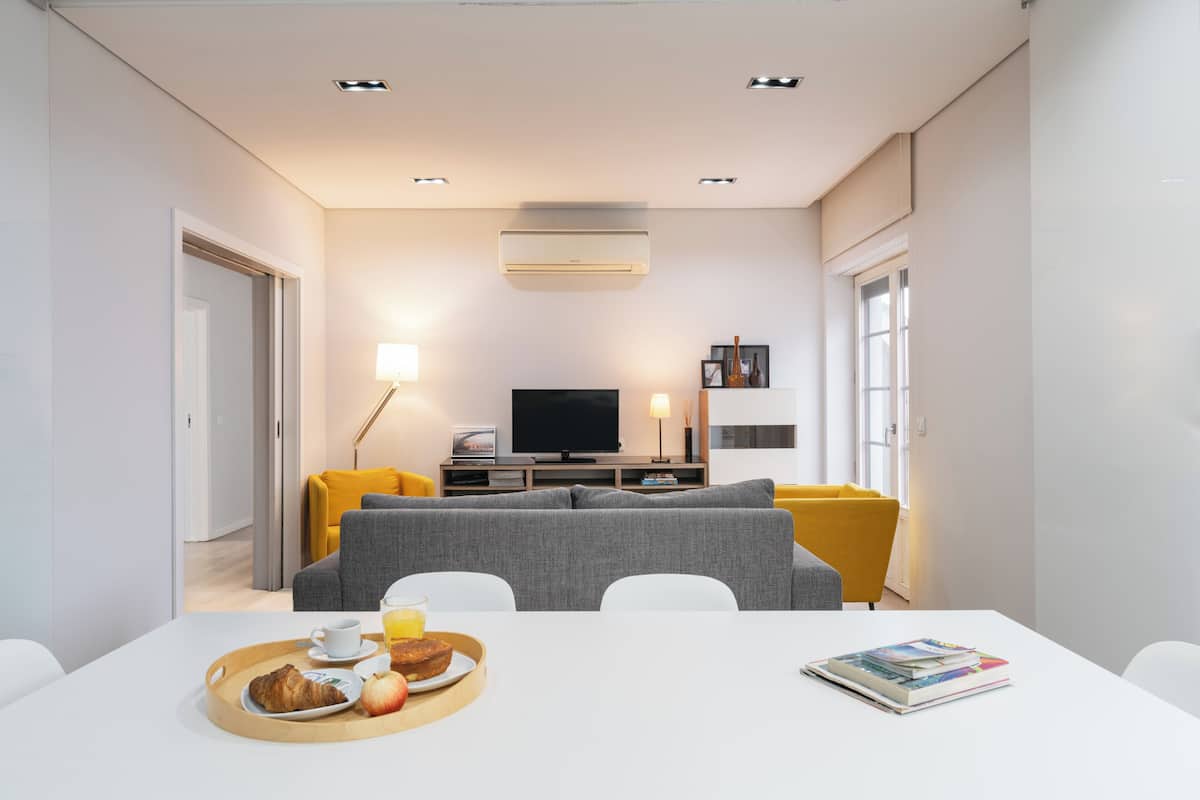 Ein modernes Wohnzimmer mit einer Couch, einem Esstisch mit Frühstück, einem Fernseher und einem Bücherregal.