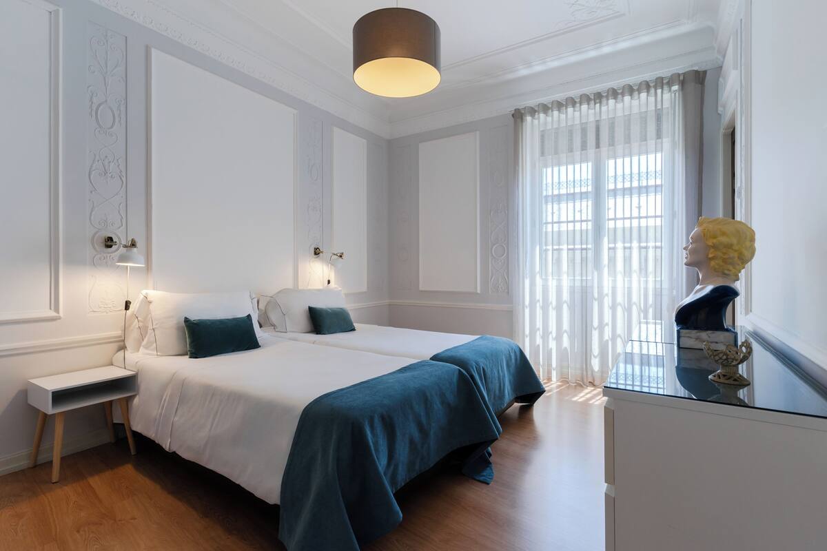 Ein Hotelzimmer mit Bett, Nachttisch, Lampe und einer Büste auf einem Schminktisch.