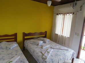 A room with two beds, yellow walls, a ceiling fan, an air conditioning unit, and a window with curtains. - Pousada Casa do Mar (Paraty)