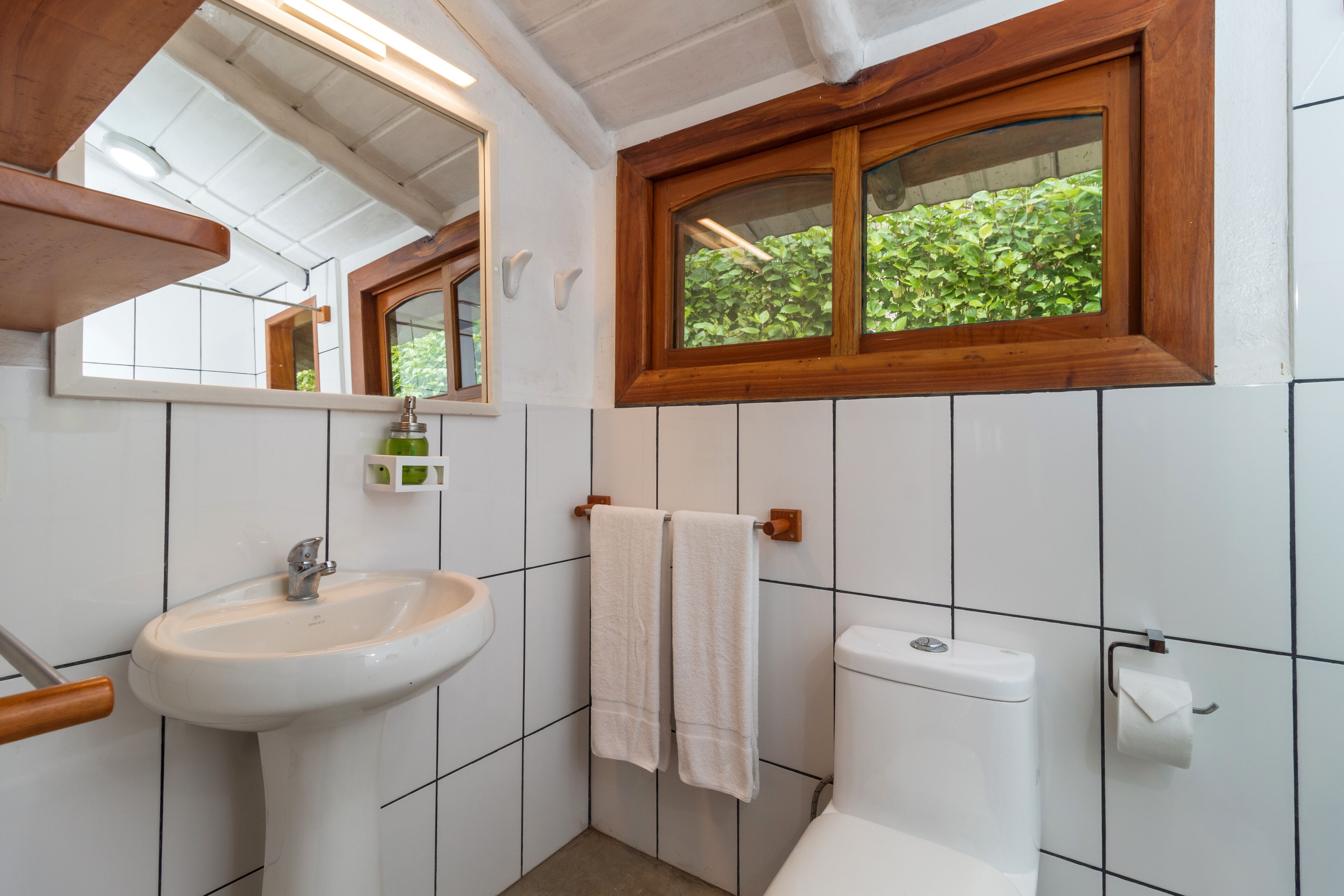 Un baño con un lavamanos blanco, un marco de ventana de madera y un inodoro.
