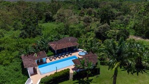 Vista aérea de una villa con piscina, rodeada de exuberante vegetación y vistas al océano.