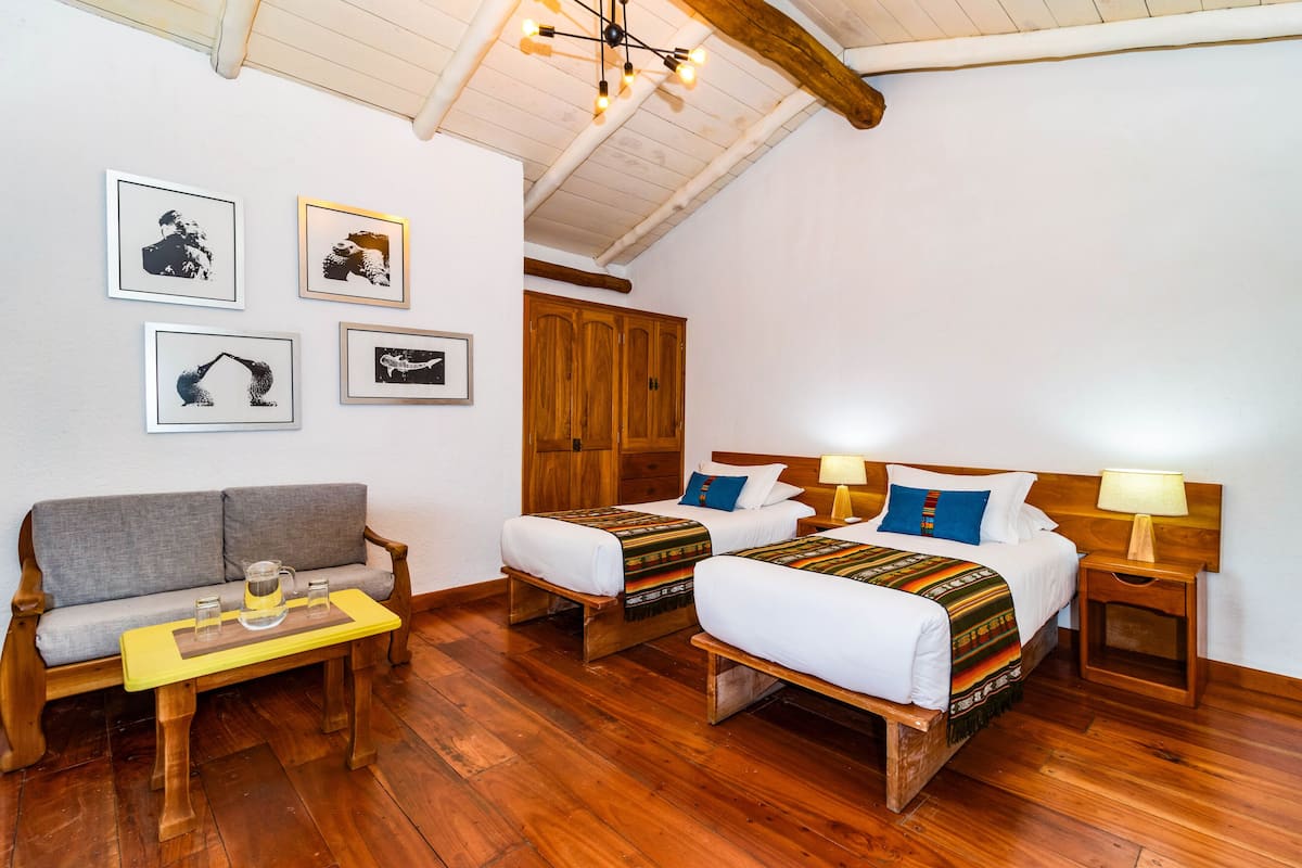 A room with two beds, a sofa, and a small table with glasses and a pitcher.