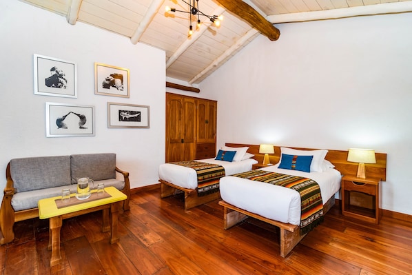 Una habitación con dos camas, un sofá y una pequeña mesa con vasos y una jarrón.