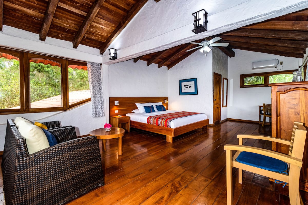 A bedroom with a wooden bed, a wicker sofa, a wooden chair, and a small table.