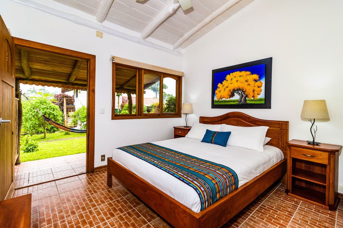 A bedroom with a large bed, wooden headboard, two bedside tables, a nightstand, a window, and a door leading to a balcony.