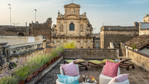 A rooftop terrace with wicker furniture, a small table with drinks, and a view of a historic church. - Palazzo Guido Boutique Hotel (Lecce)