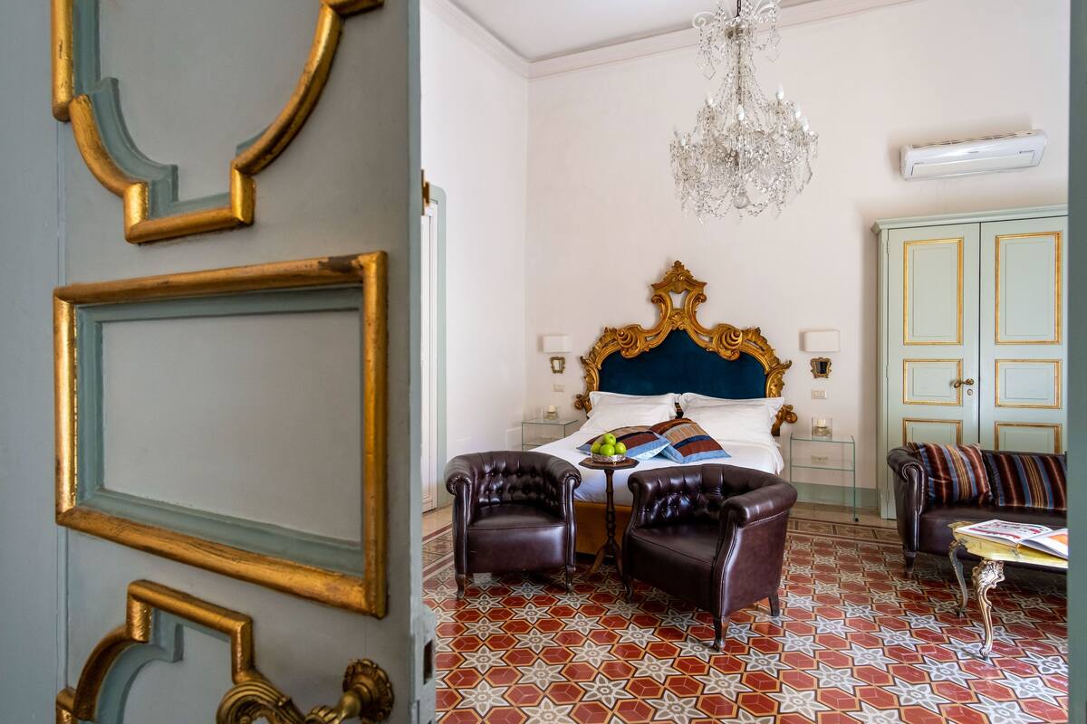 Un dormitorio con una cama grande, dos sillones, una mesita de centro, una araña y un piso con diseño.