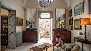 A spacious living room with a chandelier, a sofa, a coffee table, and a view into the dining area. - Palazzo Guido Boutique Hotel (Lecce)