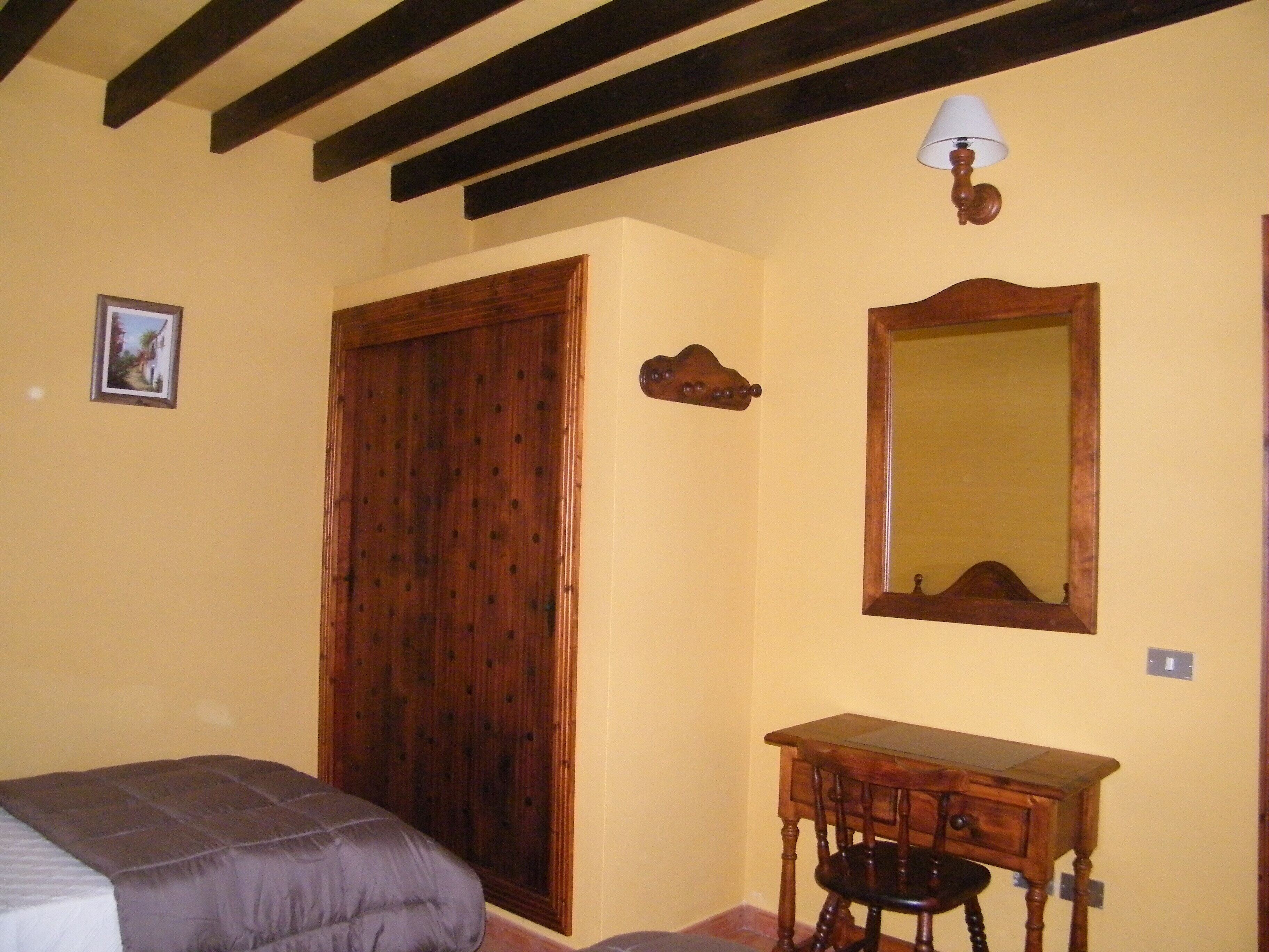 Una camera da letto con un letto, un armadio in legno, un tavolino, uno specchio e una lampada a parete.