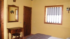 A bedroom with a bed, a desk, a chair, a window with bars, and a mirror. - SAN JOSÉ RURAL HOUSE  (Yaco)