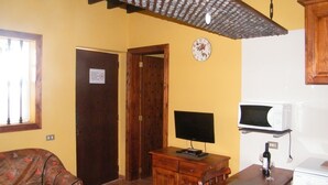 A living room with a sofa, a wooden table with a television, a clock, and a kitchen area with a microwave and stove. - SAN JOSÉ RURAL HOUSE  (Yaco)