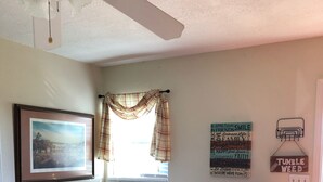 A living room with a brown leather sofa, two patterned cushions, a framed picture, a window with plaid curtains, and motivational wall art. - Tumble Weed Cabin of Lonesome Wind Ranch (Floresville)