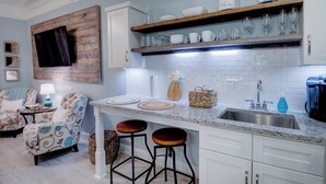 Una cocina con alacenas blancas, encimera de granito, un espacio para vinos empotrado y un televisor montado en una pared de madera.