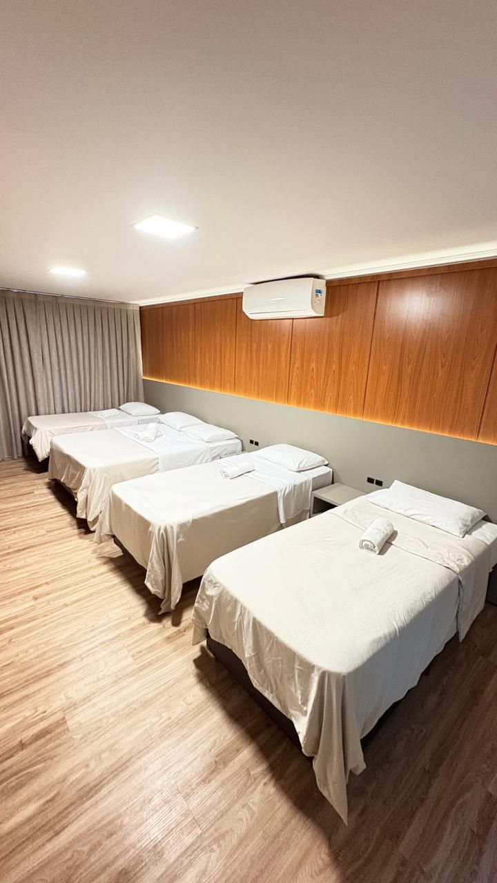 A hotel room with four single beds, a wooden headboard, an air conditioning unit, and a wooden floor.