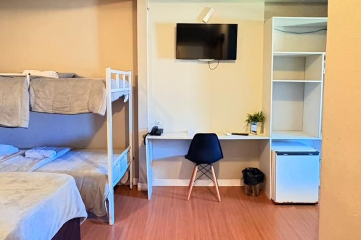 A room with a bunk bed, a desk with a chair, a TV, and a shelving unit.