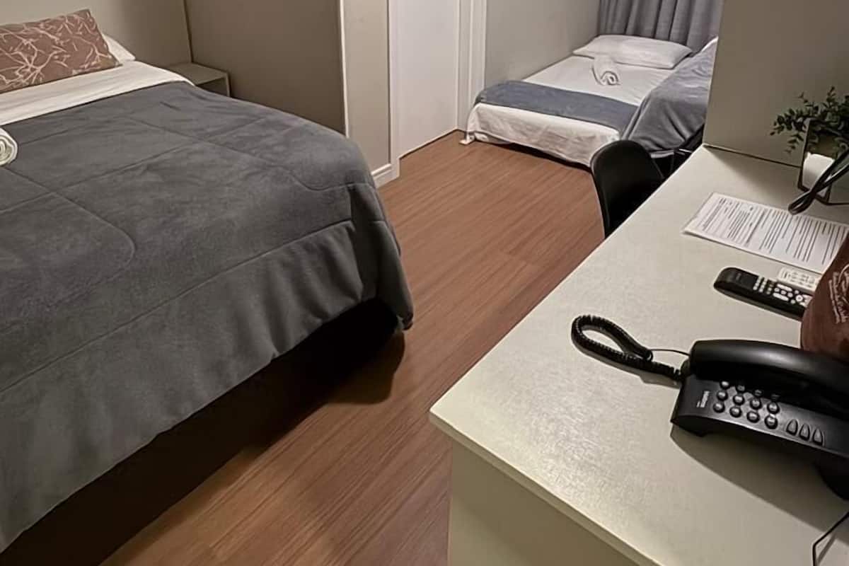 A hotel room with a bed, a desk with a phone, and a door.