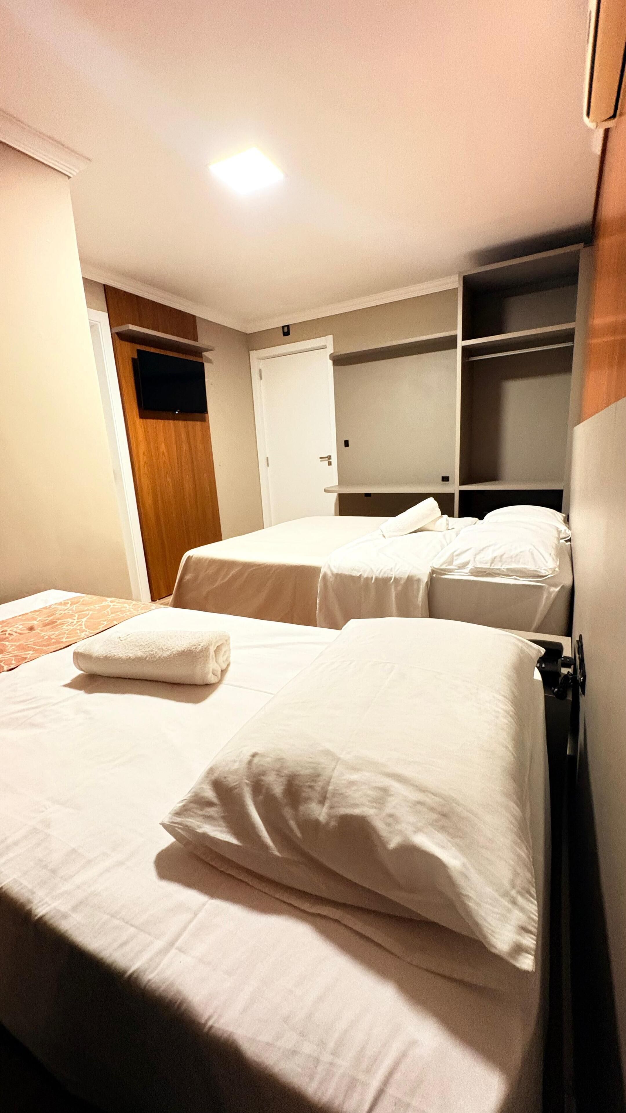 Une chambre d’hôtel avec deux lits, un téléviseur fixé au mur et une armoire.