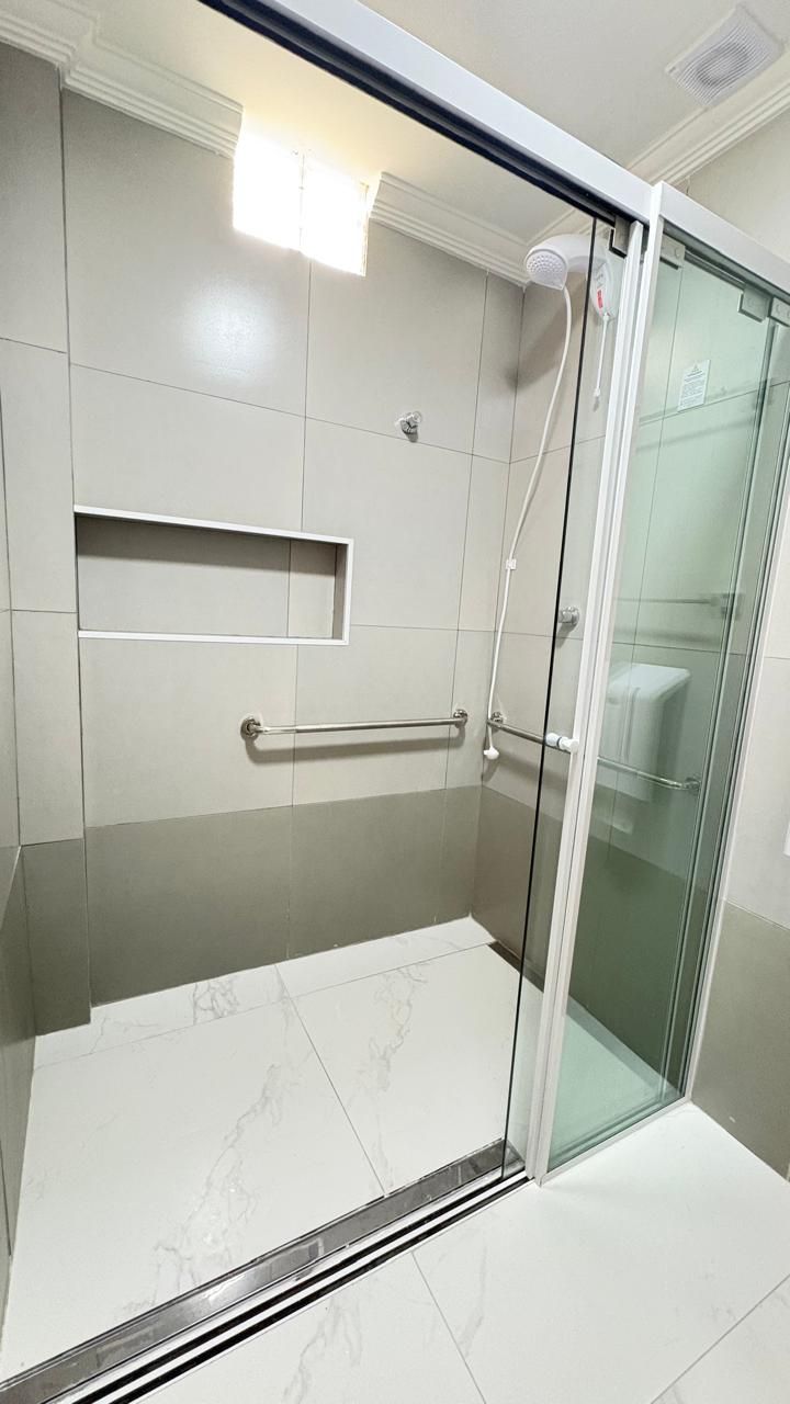 A modern bathroom with a glass shower enclosure, a handrail, and a small shelf.