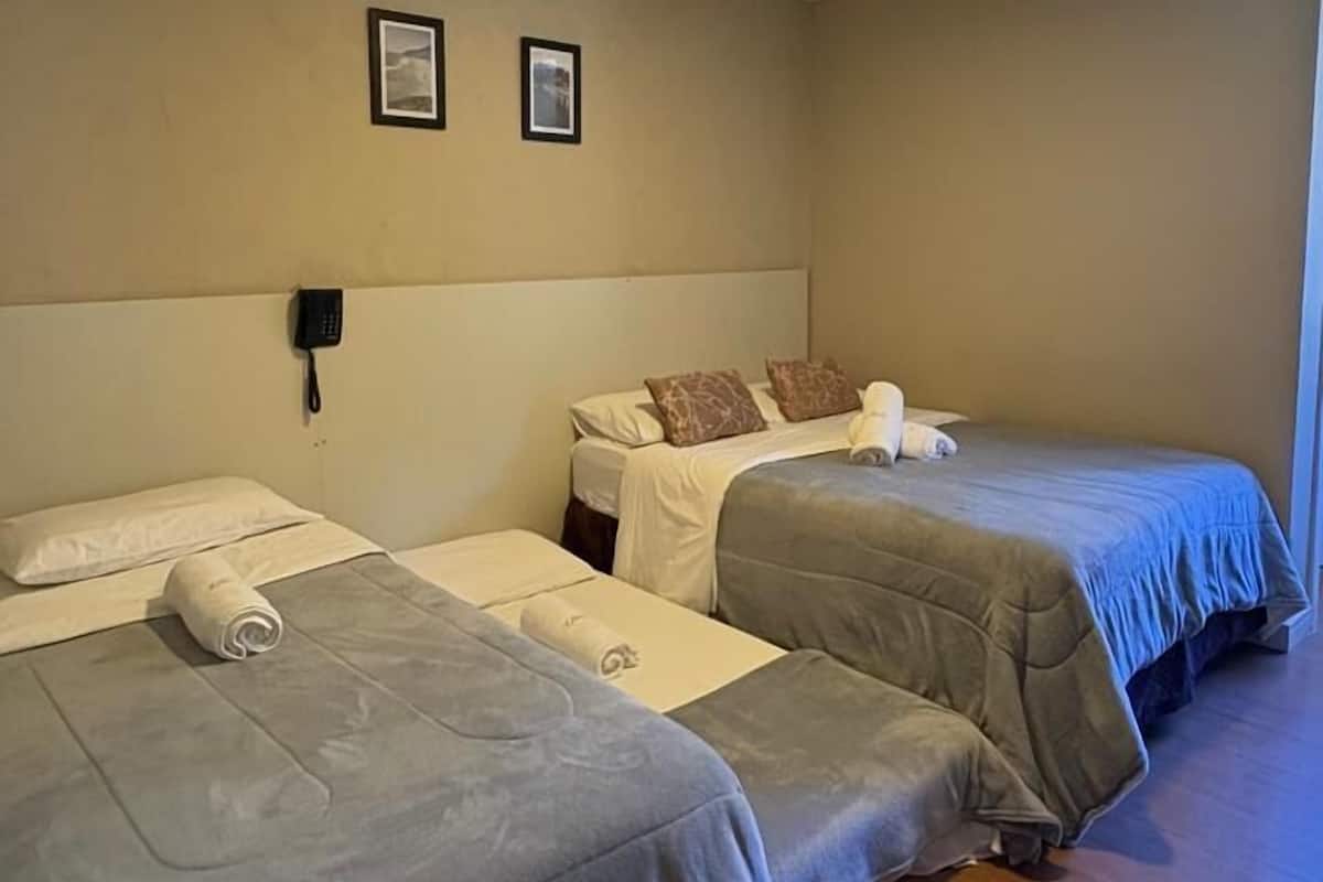 A hotel room with two beds, a phone on the wall, and a ceiling light.