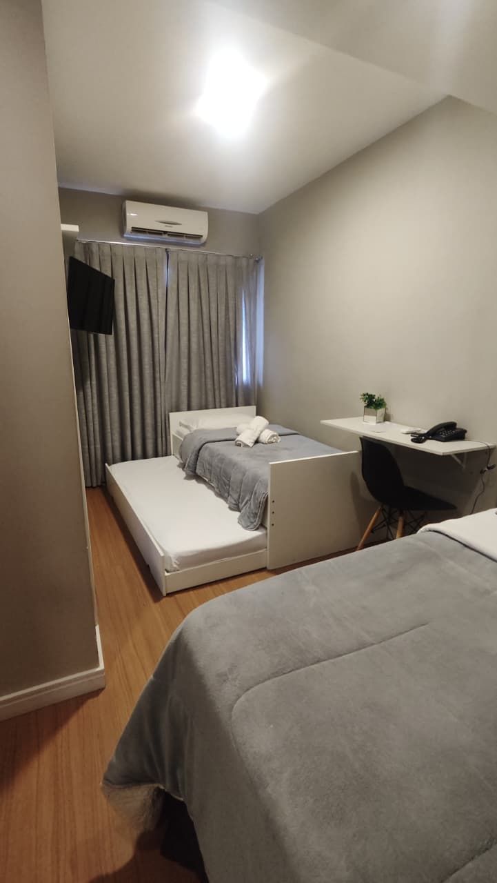 A compact hotel room with a bed, a desk, and an air conditioning unit.
