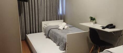 A compact hotel room with a bed, a desk, and an air conditioning unit.