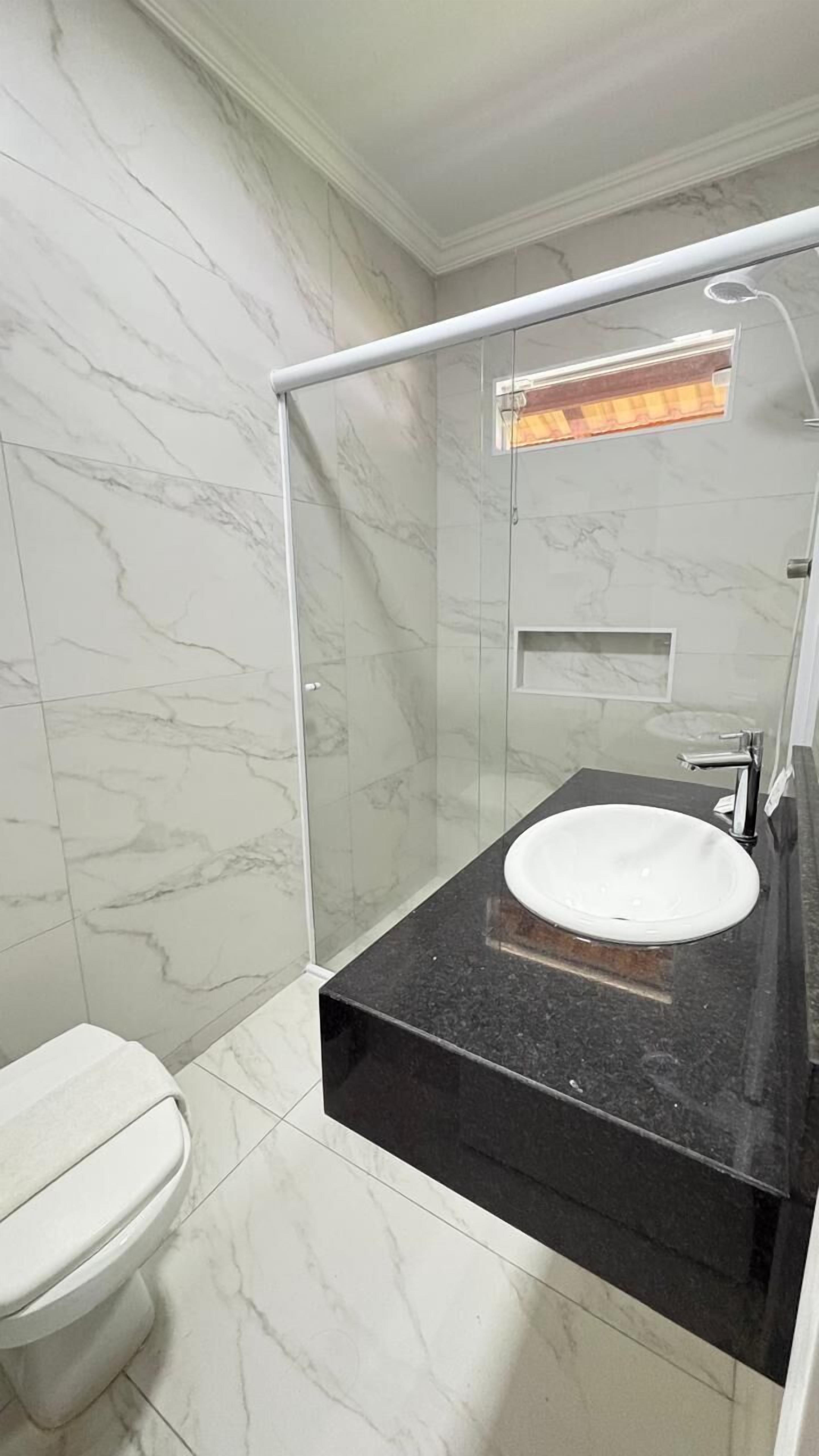 A bathroom with a white toilet, a black countertop sink, and a glass-enclosed shower area.