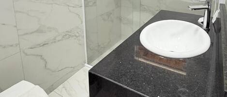 A bathroom with a white toilet, a black countertop sink, and a glass-enclosed shower area.