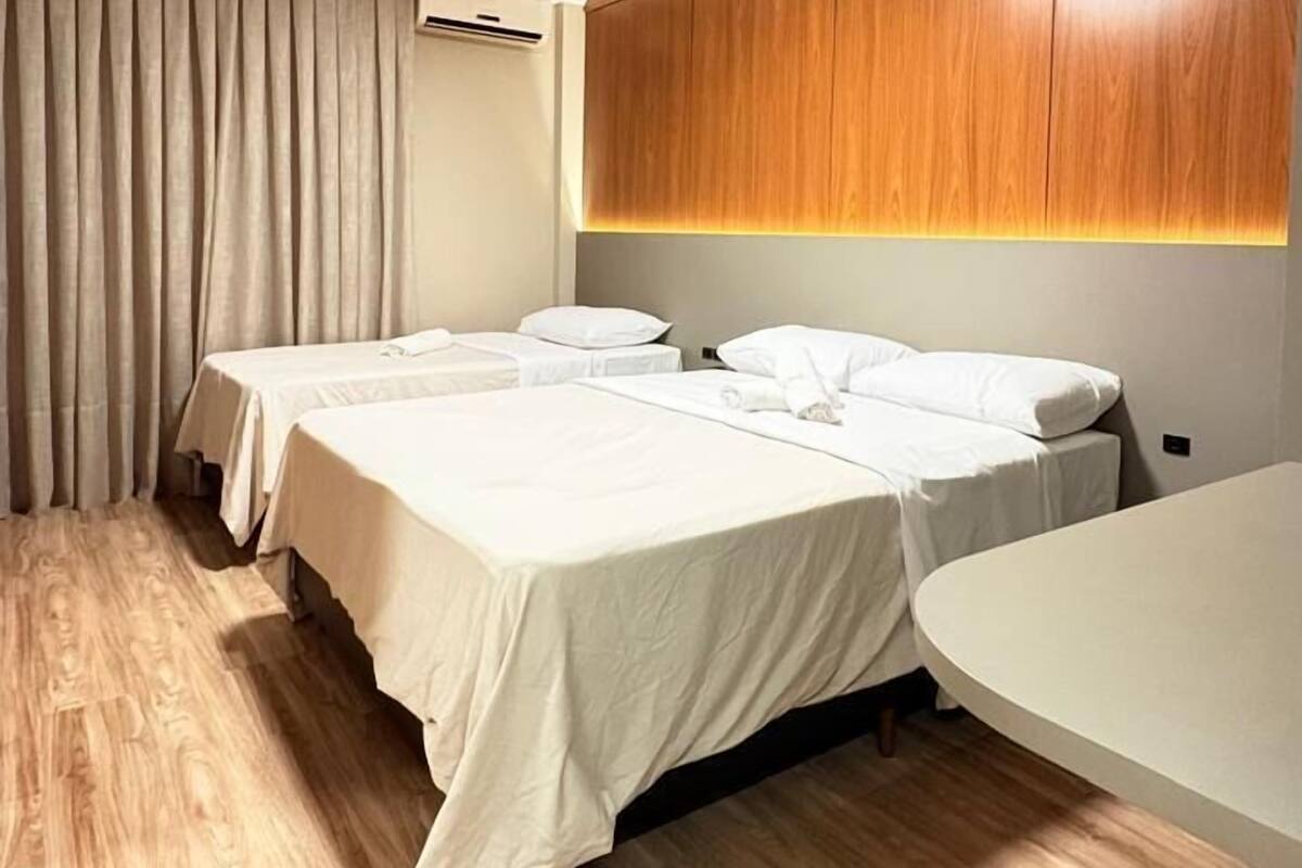 A hotel room with two beds, a wooden headboard, a round table, and a curtain.