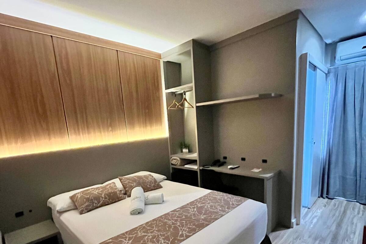 A hotel room with a large bed, a bedside table, a mirror, a desk, and a chair.